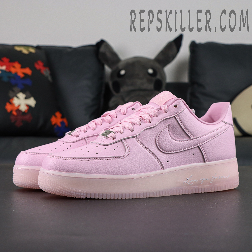 Angled front view of NOCTA x Nike Air Force 1 “Pink Foam” showing soft pink tone and metallic lace tag.